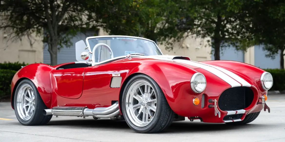 1965 Ford Backdraft Cobra Replika in rot mit weißen Streifen, aufgenommen auf einem Parkplatz.