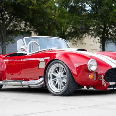 1965 Ford Backdraft Cobra Replika in rot mit weißen Streifen, aufgenommen auf einem Parkplatz.