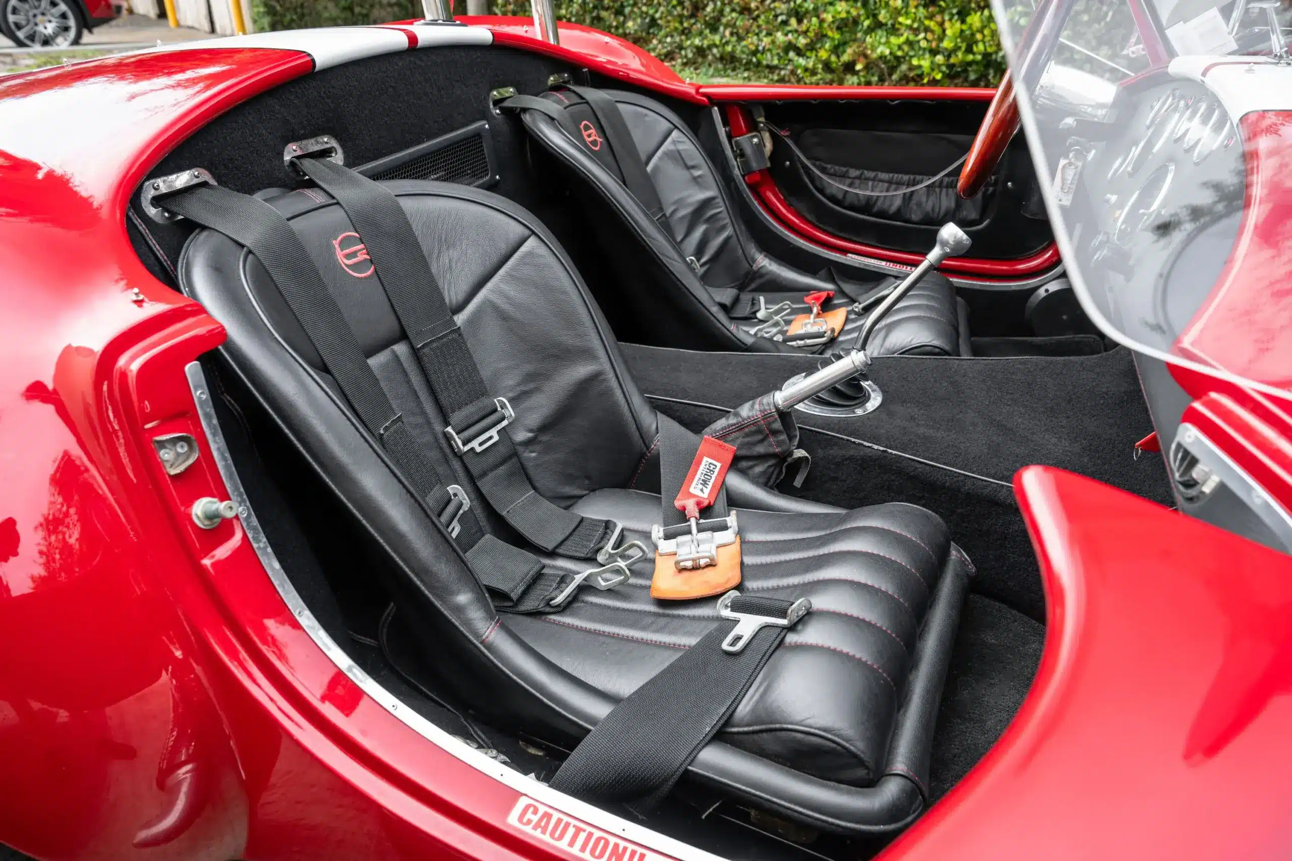 Innenraum einer 1965 Ford Backdraft Cobra mit schwarzen Ledersitzen, roten Nähten und Vierpunktgurten