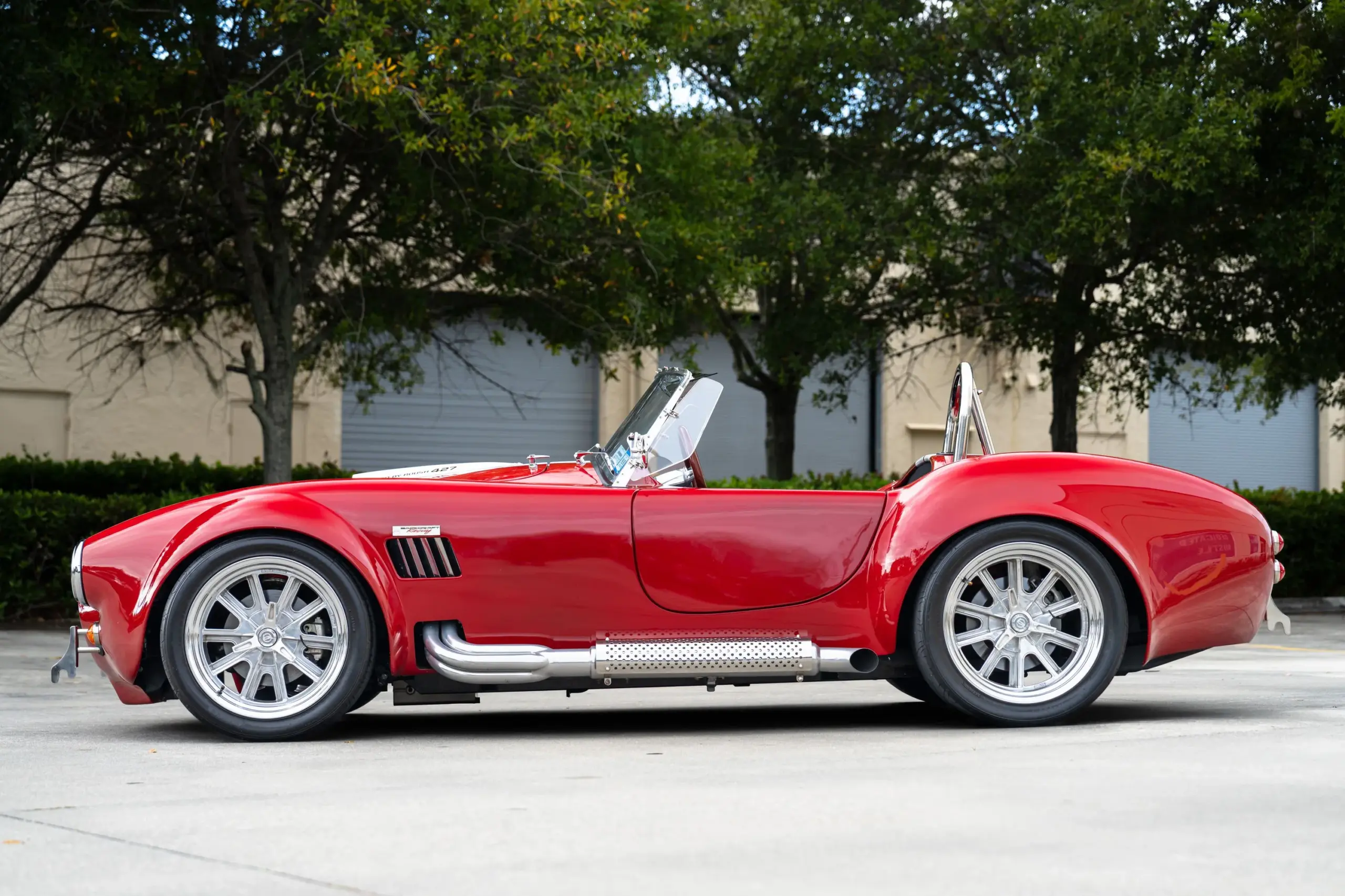 Seitenansicht einer roten 1965 Ford Backdraft Cobra mit weißen Rennstreifen und verchromten Komponenten.