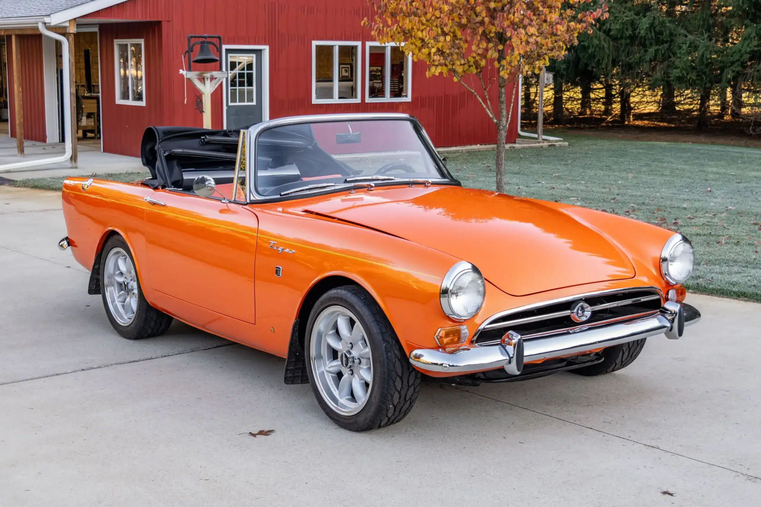 Sunbeam Tiger Mk1 Roadster von 1965 in orangefarbener Pearl-Effekt-Lackierung, Cabrioverdeck offen, geparkt vor rotem Gebäude