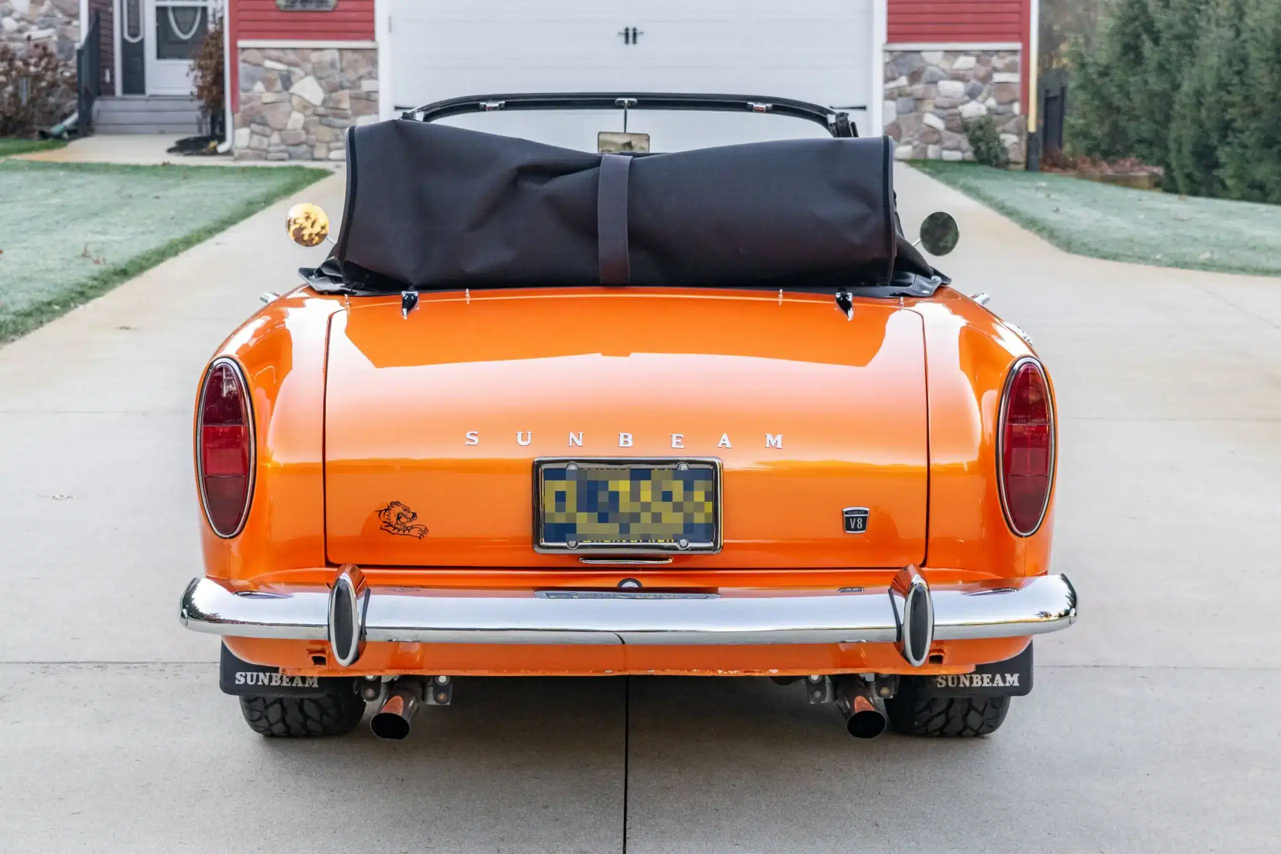 Heckansicht eines orangefarbenen Sunbeam Tiger Mk1 mit schwarzem Verdeck und doppelten Auspuffendrohren auf einer Auffahrt.