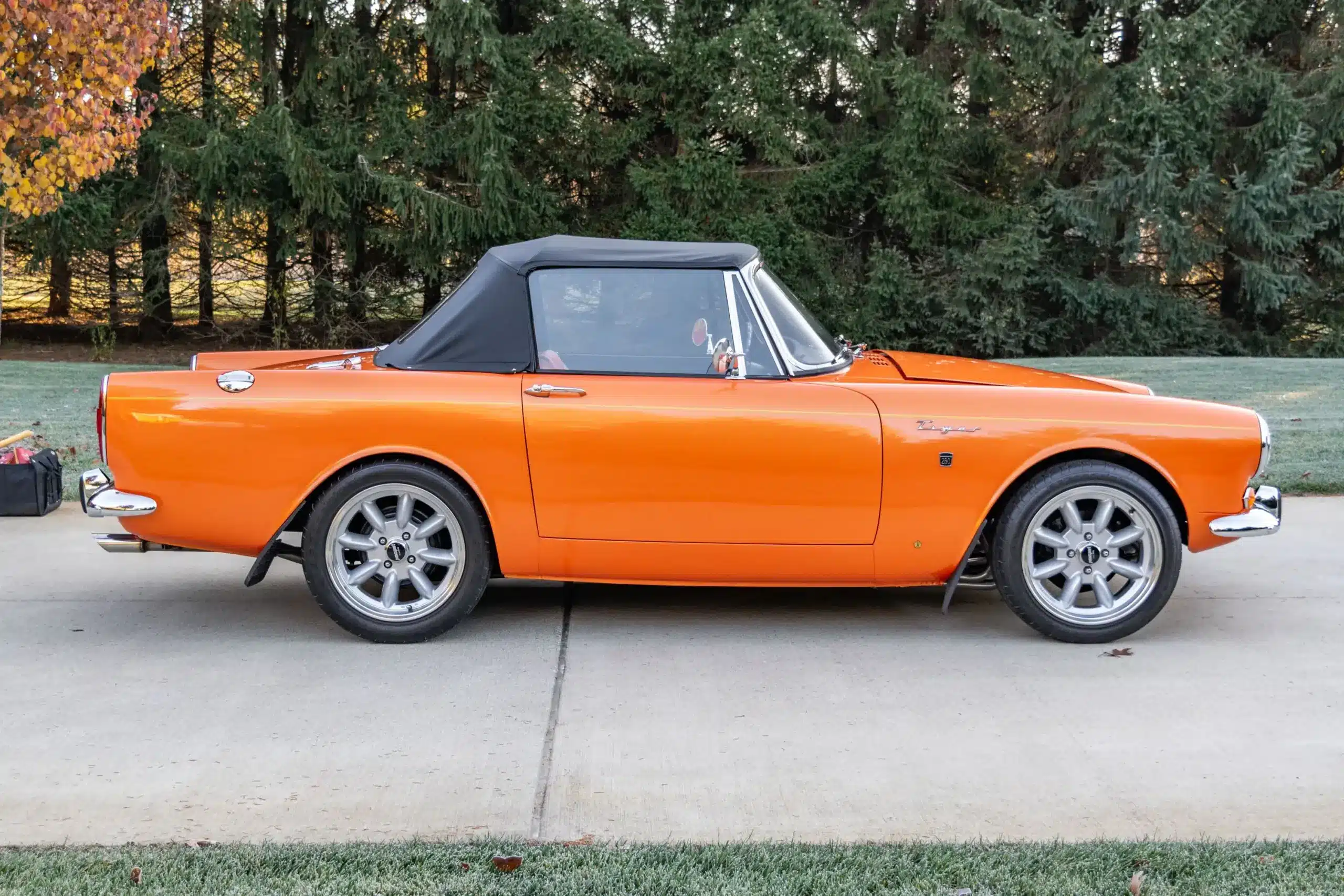 Seitenansicht eines orangefarbenen Sunbeam Tiger Mk1 aus dem Jahr 1965 mit schwarzem Stoffverdeck und modernen Felgen.