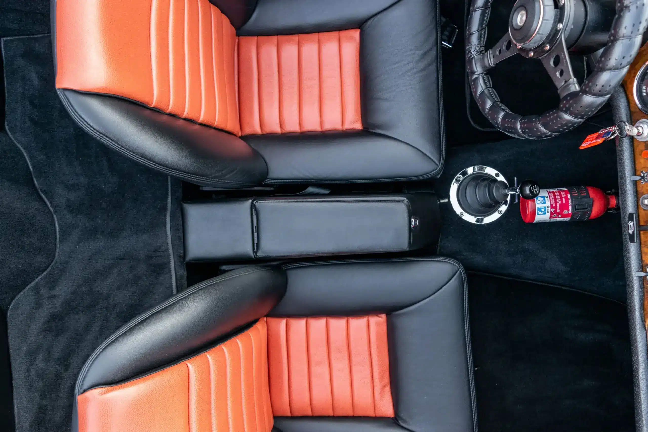 Blick von oben auf die orange-schwarzen Ledersitze, das Lederlenkrad und die Mittelkonsole eines Sunbeam Tiger Mk1.