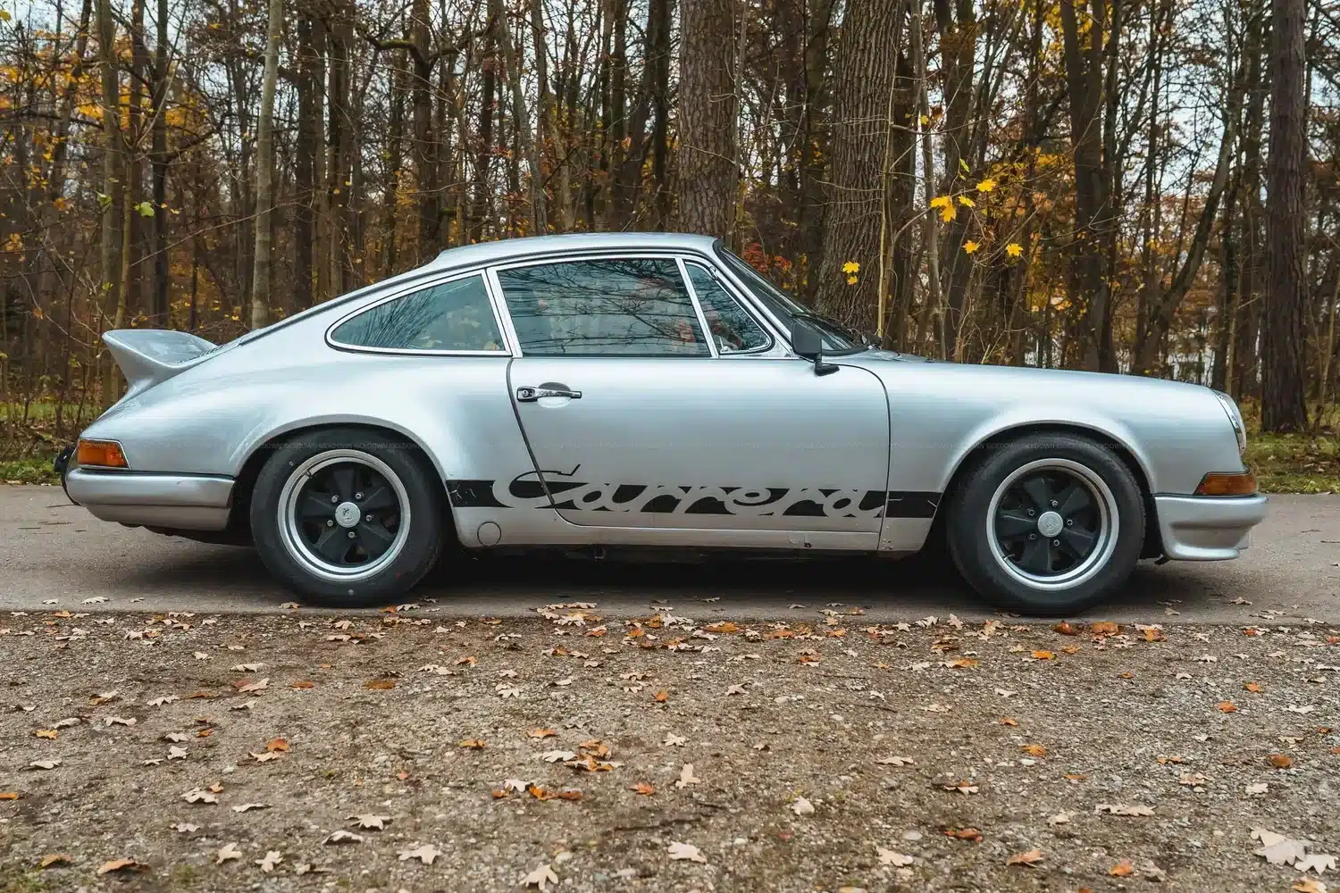Silberner 1967 Porsche 911 S SWB mit Carrera-Schriftzug, RS-Heckspoiler und Fuchs-Felgen vor herbstlichem Wald.