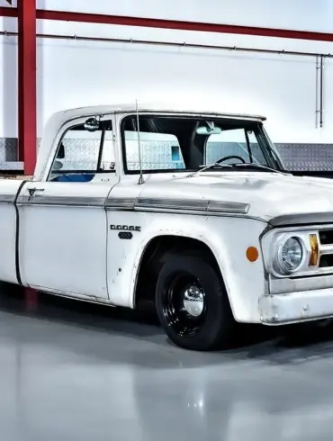 Seitenansicht eines weißen Dodge D100 Pickups von 1968 mit originaler Lackierung und altersbedingter Patina, geparkt in einer hellen Halle.