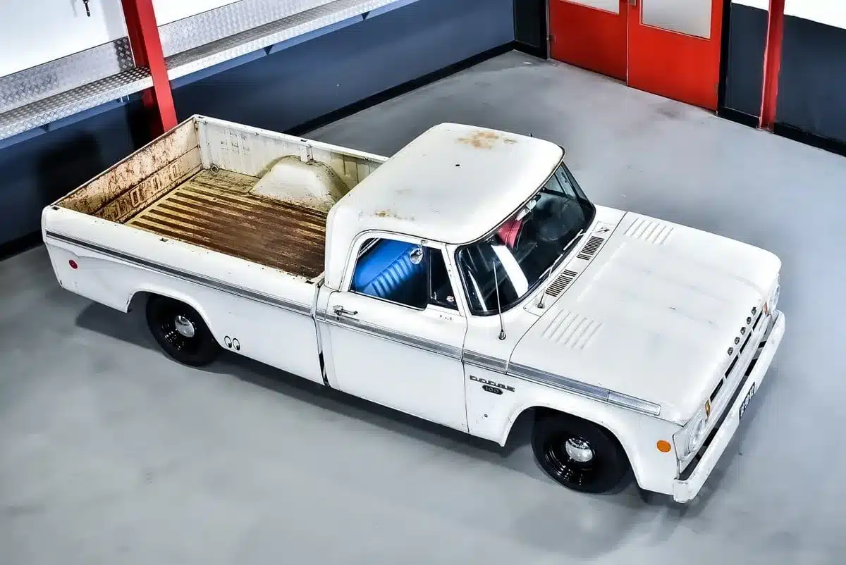 Weißer Dodge D100 Pickup aus dem Baujahr 1968 mit authentischer Patina, fotografiert aus erhöhter Perspektive in einer modernen Halle.