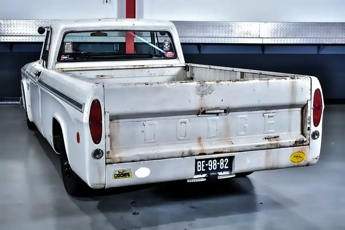 Heckansicht eines weißen Dodge D100 Pickups von 1968 mit sichtbarer Patina in einer Halle.