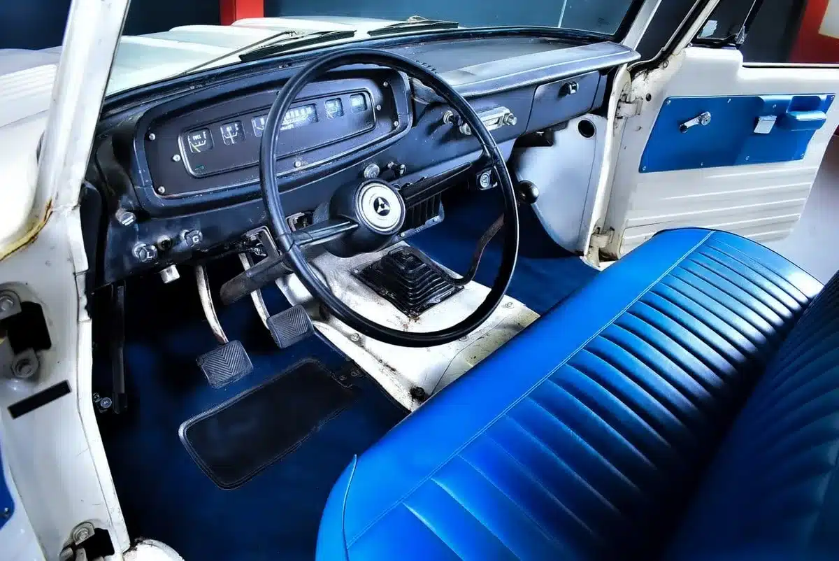 Innenraum eines 1968 Dodge D100 mit Armaturenbrett, großem Lenkrad und blauer Sitzbank.