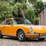 Gelber Porsche 911 T Sportomatic Baujahr 1969, Frontansicht, geparkt vor einem Backsteingebäude.