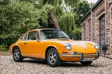 Gelber Porsche 911 T Sportomatic Baujahr 1969, Frontansicht, geparkt vor einem Backsteingebäude.