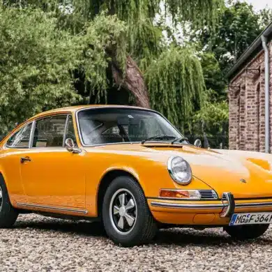 Gelber Porsche 911 T Sportomatic Baujahr 1969, Frontansicht, geparkt vor einem Backsteingebäude.