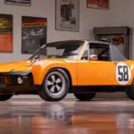 Gelber Porsche 914/6 R von 1970 mit Startnummer 58 in einer Garage, umgeben von Motorsport-Postern.