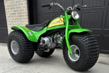 Grünes dreirädriges Honda ATC 90 Geländefahrzeug aus dem Jahr 1972, stehend auf Beton vor schwarzem Garagentor