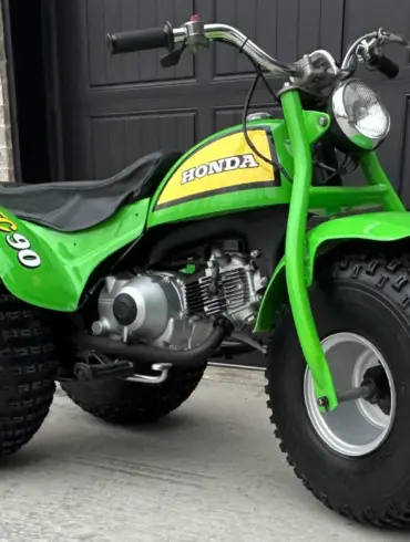 Grünes dreirädriges Honda ATC 90 Geländefahrzeug aus dem Jahr 1972, stehend auf Beton vor schwarzem Garagentor