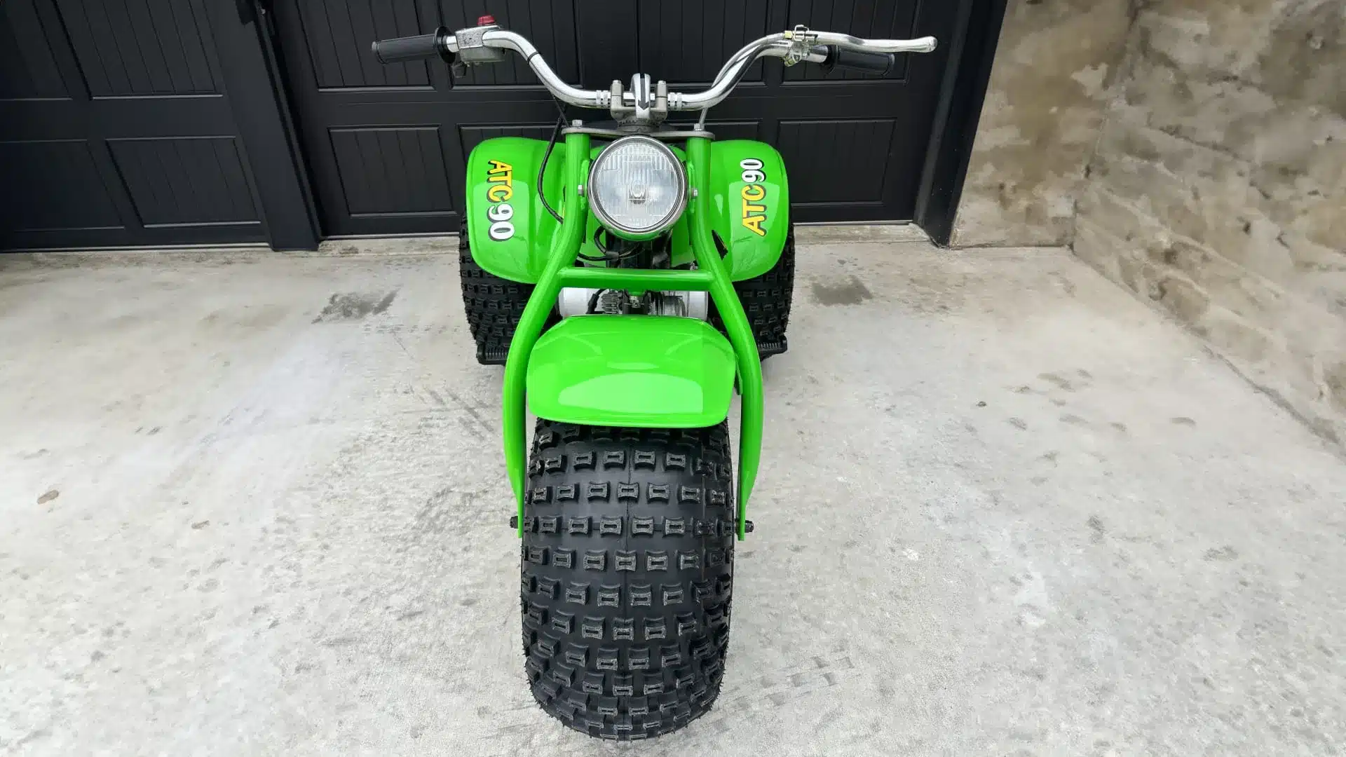 Frontansicht der 1972 Honda ATC 90 mit breiten Ballonreifen und grüner Verkleidung, fotografiert vor einer Garage.