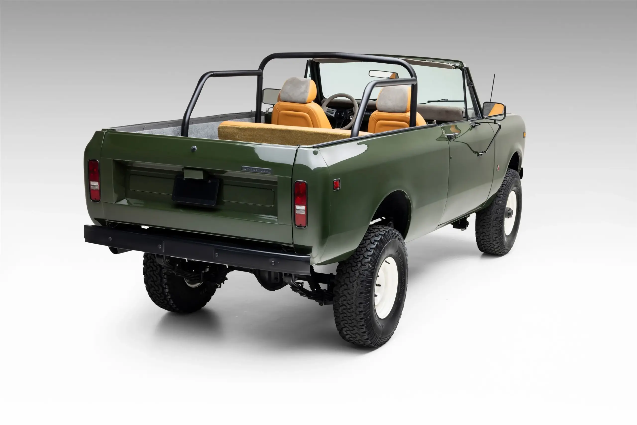 1978 International Harvester Scout II Traveler in Dunkelgrün, offen ohne Dach, mit Überrollbügel, weißen Felgen und beigen Sitzen, seitlich-hinten fotografiert.