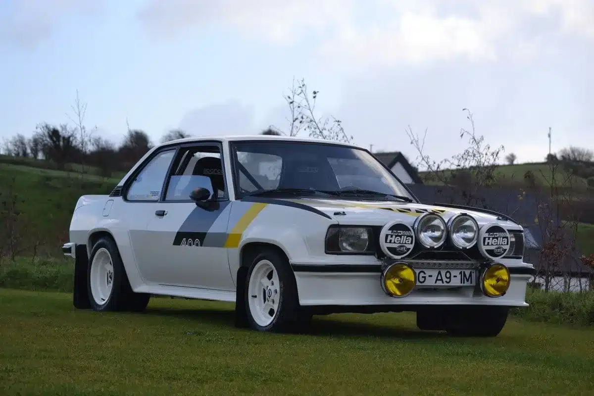 Seitenansicht eines Opel Ascona 400R von 1980 mit Hella Zusatzscheinwerfern, Rallye-Design und weißer Lackierung auf einer Wiese.