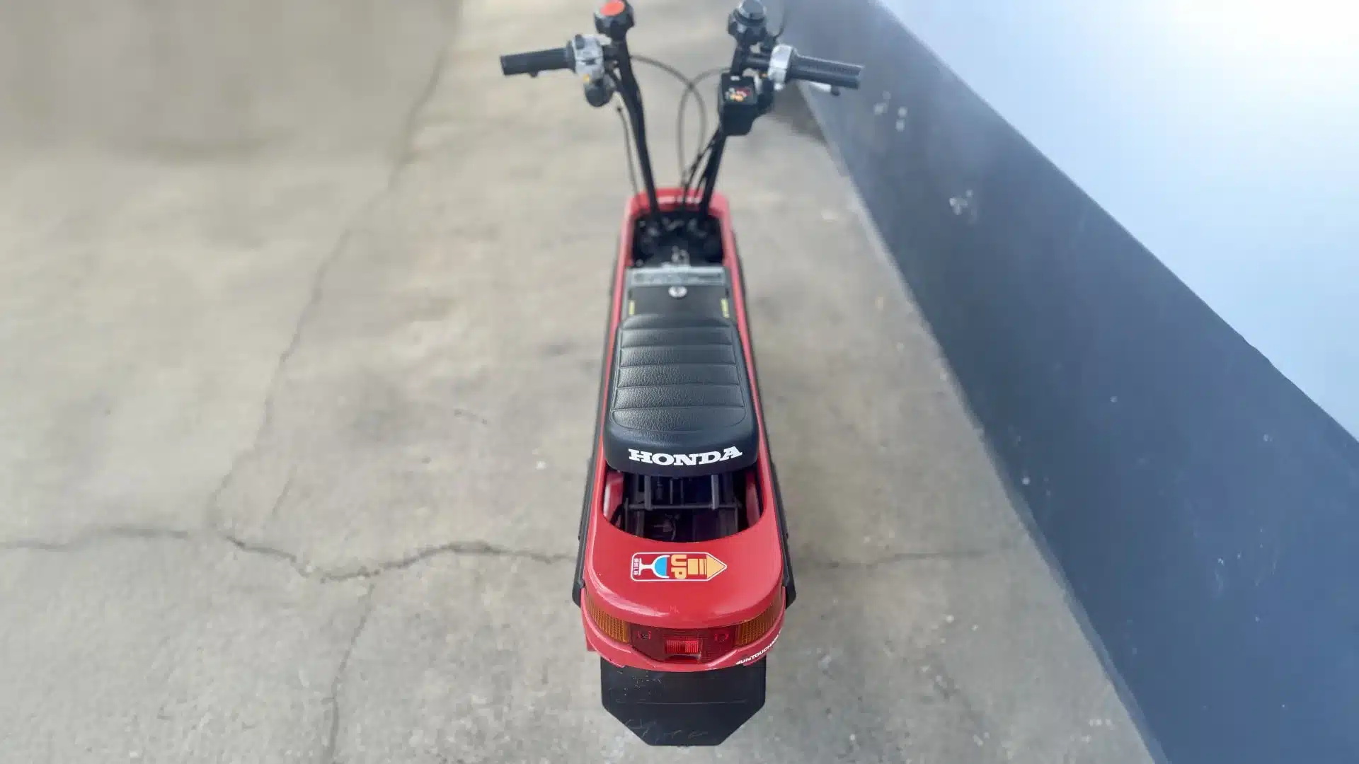 Blick von oben auf einen roten Honda Motocompo Roller mit schwarzem Sitz und sichtbarem Lenker.