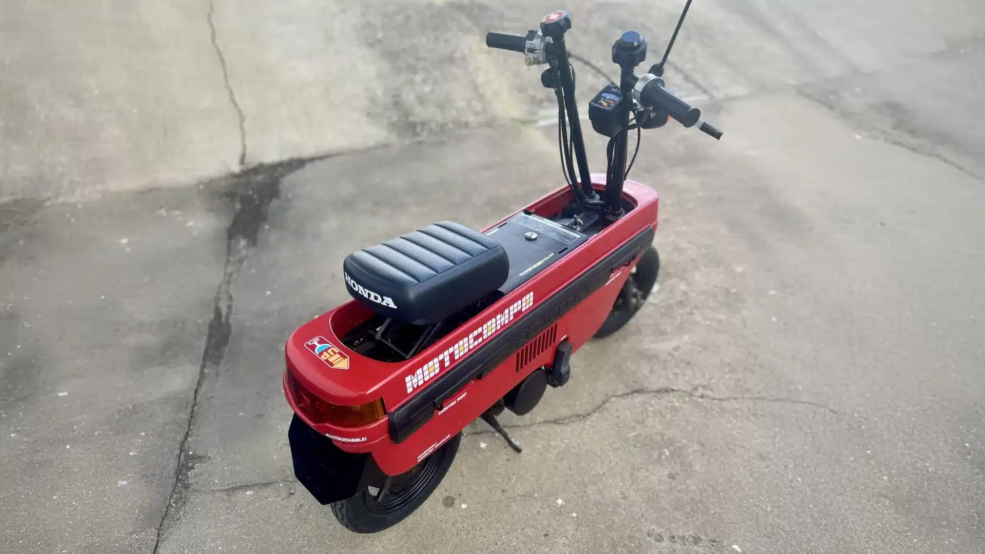 Roter Honda Motocompo Roller von 1982, kompakter faltbarer City-Scooter, abgestellt auf einer Betonfläche.