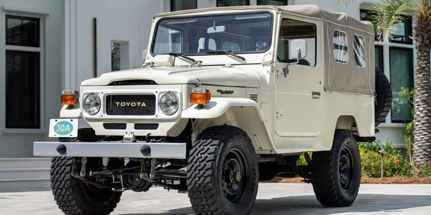 Restaurierter Toyota Land Cruiser FJ43 von 1982 in Weiß, mit beigem Softtop und Offroad-Bereifung, steht geparkt vor einer modernen Villa.