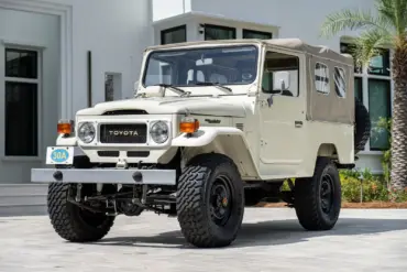 Restaurierter Toyota Land Cruiser FJ43 von 1982 in Weiß, mit beigem Softtop und Offroad-Bereifung, steht geparkt vor einer modernen Villa.
