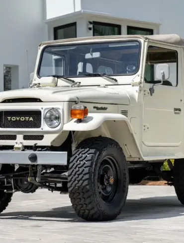 Restaurierter Toyota Land Cruiser FJ43 von 1982 in Weiß, mit beigem Softtop und Offroad-Bereifung, steht geparkt vor einer modernen Villa.