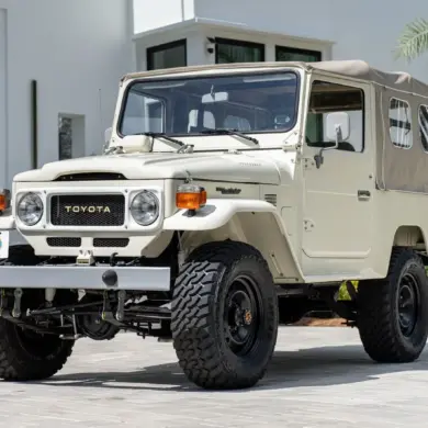 Restaurierter Toyota Land Cruiser FJ43 von 1982 in Weiß, mit beigem Softtop und Offroad-Bereifung, steht geparkt vor einer modernen Villa.