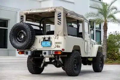 Rückansicht eines weißen Toyota Land Cruiser FJ43 aus dem Jahr 1982 mit beigem Softtop und Ersatzrad.