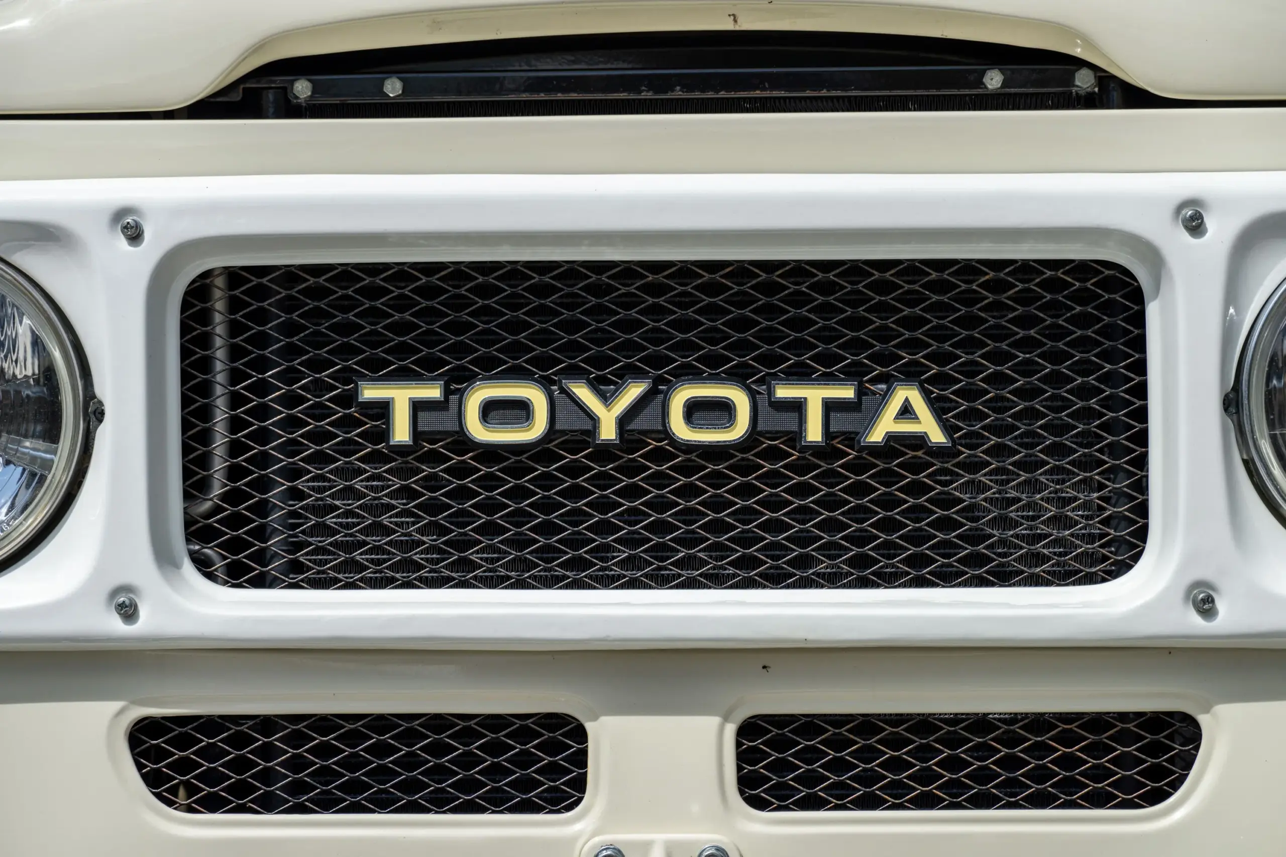 Weißer Kühlergrill eines Toyota Land Cruiser FJ43 von 1982 mit markantem TOYOTA-Schriftzug und Scheinwerfern.
