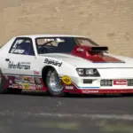 1984 Chevrolet Camaro Pro Stock Dragster Rennauto mit Sponsorenlogos, gebaut von Reher-Morrison und gefahren von Lee Shepherd, steht schräg vor einer Backsteinwand