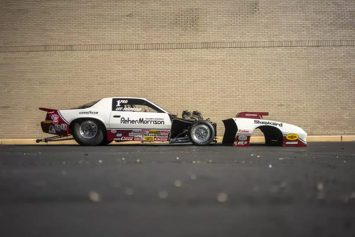 Seitenansicht eines 1984 Chevrolet Camaro Pro-Stock-Rennwagens von Lee Shepherd mit abgenommener Frontverkleidung vor einer Backsteinwand.