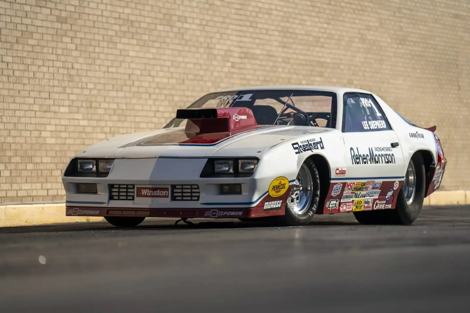 Weiße Pro Stock Rennversion eines 1984 Chevrolet Camaro mit Sponsorenaufklebern und auffälligem Lufteinlass auf der Motorhaube.