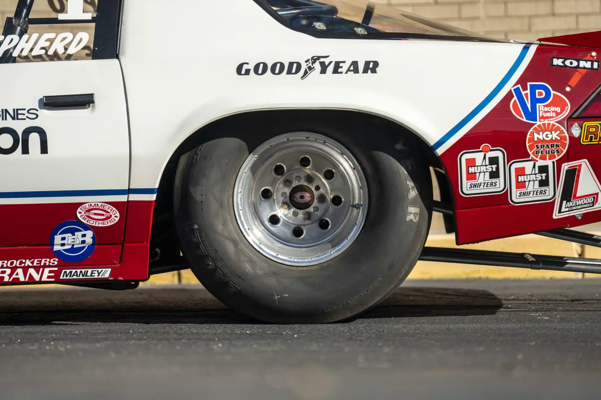Nahaufnahme des Hinterrads und Seitenteils eines mit Sponsoren versehenen 1984 Chevrolet Camaro Drag-Rennwagens.