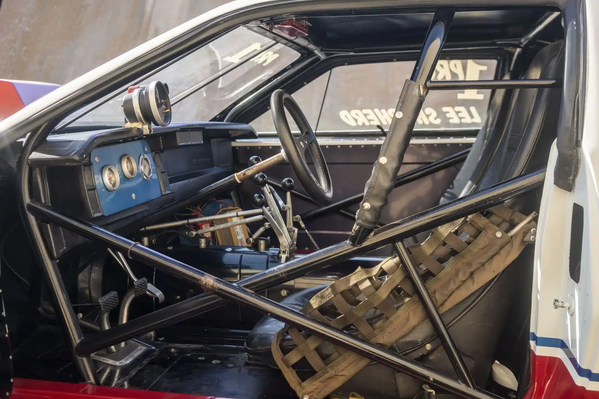 Innenraum eines 1984er Chevrolet Camaro Rennwagens mit Rennsitz, Sicherheitsnetz und umfangreicher Motorsport-Ausstattung.