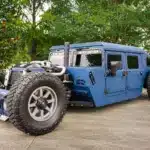 Offener, radikal umgebauter Humvee von 1987 in Blau mit markanter Schutzbeschichtung, offener Motorpräsentation und massiven Offroadreifen.