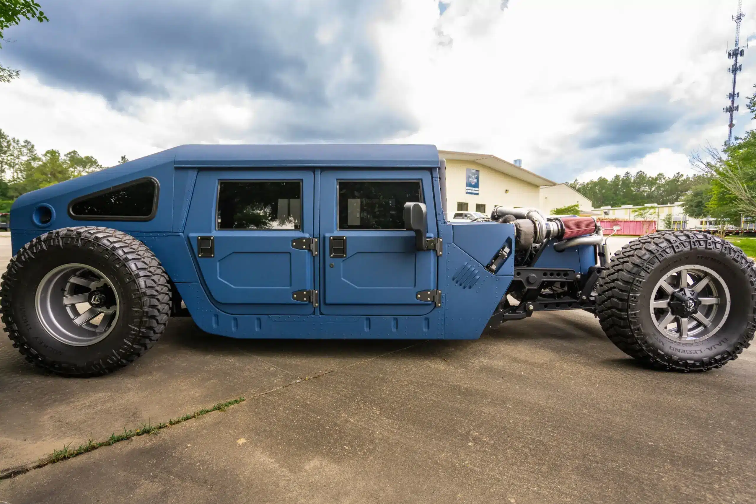 Seitenansicht eines speziell umgebauten Humvee aus dem Jahr 1987 mit blauer Schutzschicht, großen Offroad-Reifen und offen präsentiertem Motor.