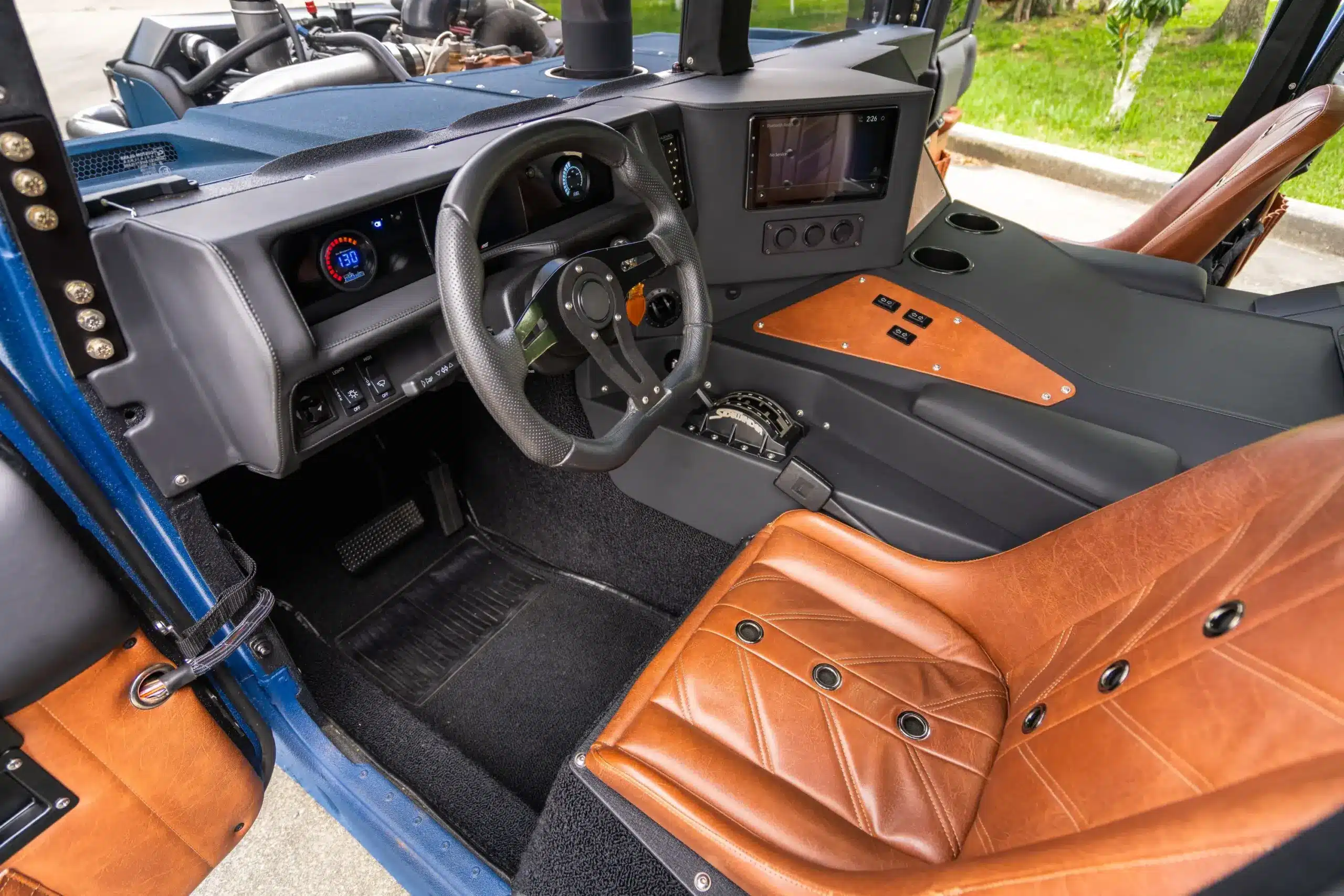 Innenraum eines individuell umgebauten Humvee von 1987 mit braunen 'bomber' Ledersitzen, schwarzem Suede-Dashboard und moderner Elektronik.