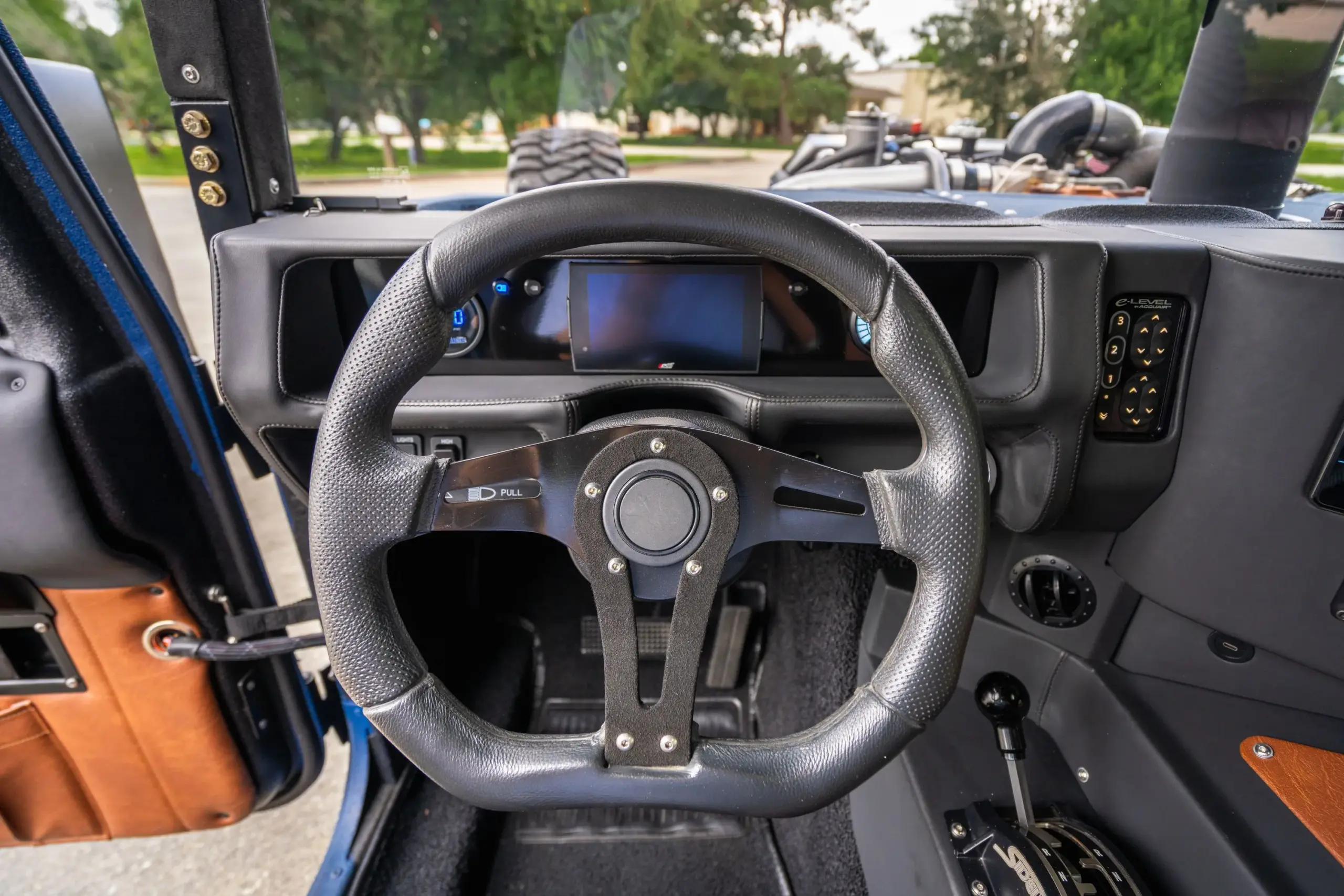 Blick auf das Lenkrad, die Mittelkonsole und digitale Anzeigen eines maßgeschneiderten Humvee mit modernem Interieur.