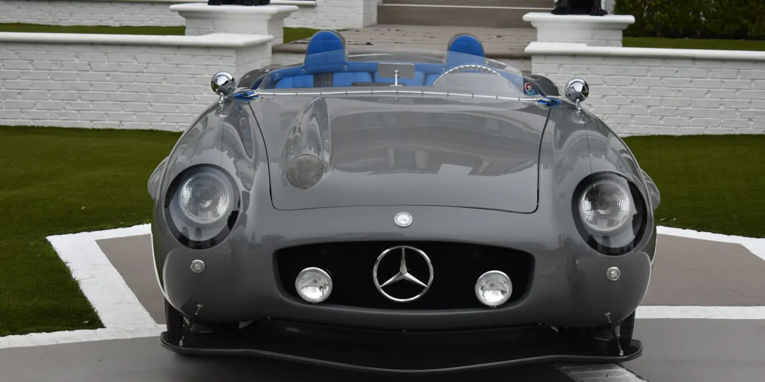 Grauer S-Klub LA Roadster, inspiriert vom Mercedes 300 SLR, mit blauen Sitzen und markanter Frontpartie, stehend vor Treppe und weißer Mauer.