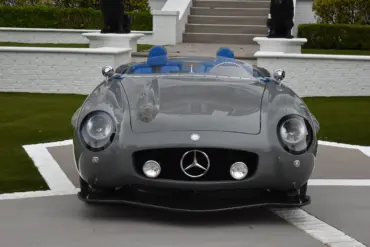 Grauer S-Klub LA Roadster, inspiriert vom Mercedes 300 SLR, mit blauen Sitzen und markanter Frontpartie, stehend vor Treppe und weißer Mauer.