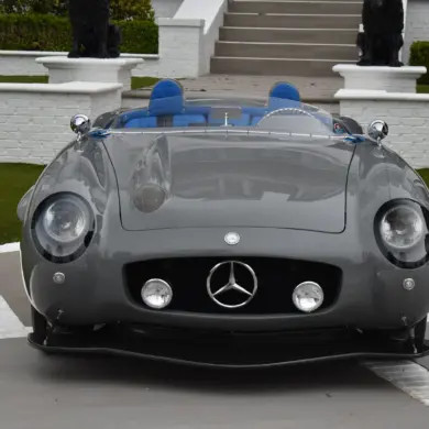 Grauer S-Klub LA Roadster, inspiriert vom Mercedes 300 SLR, mit blauen Sitzen und markanter Frontpartie, stehend vor Treppe und weißer Mauer.