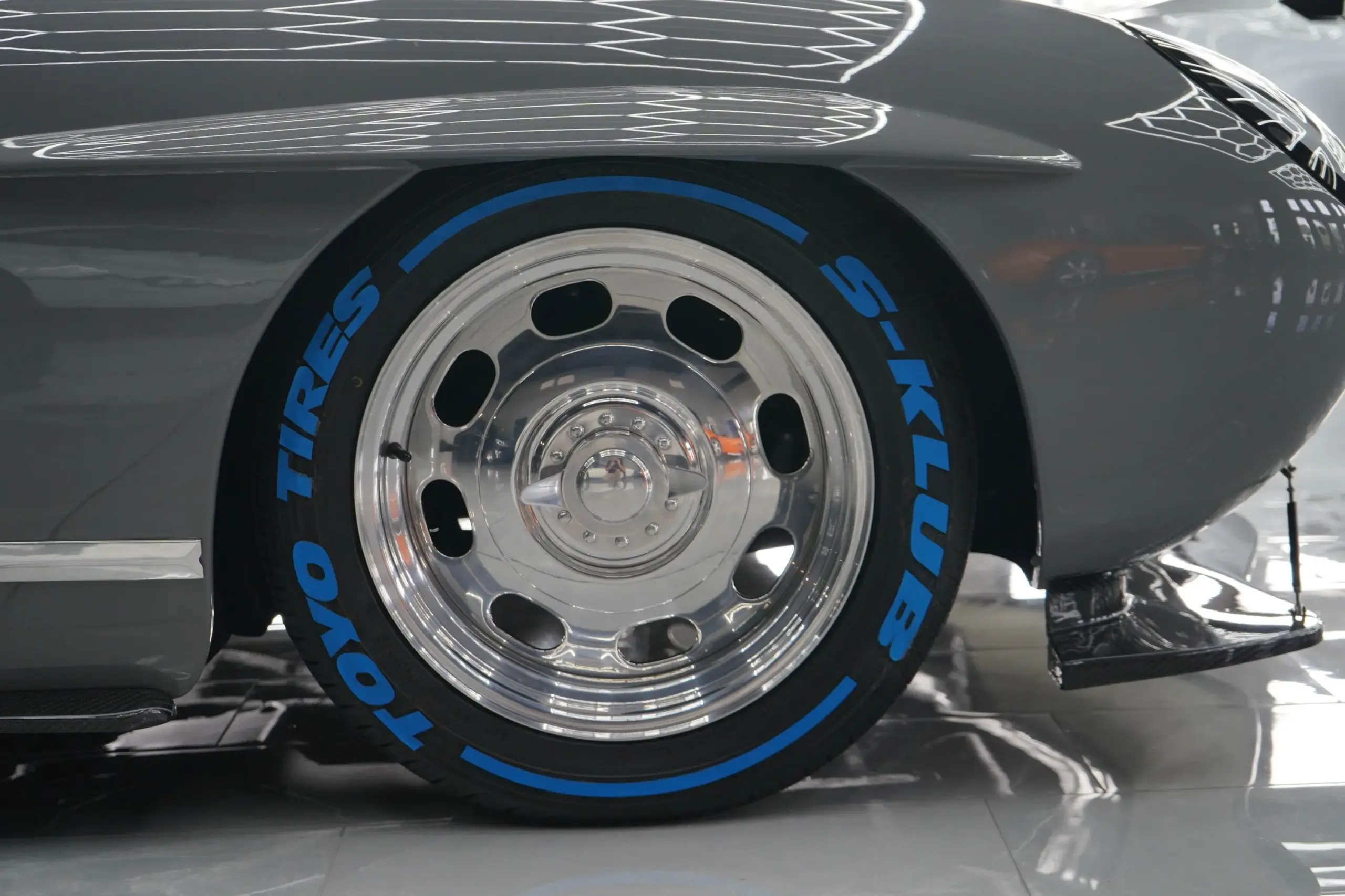 Poliertes Boyd-Coddington-Aluminiumrad mit Toyo-Bereifung und blauen S-Klub-Schriftzügen an einem exklusiven Roadster.