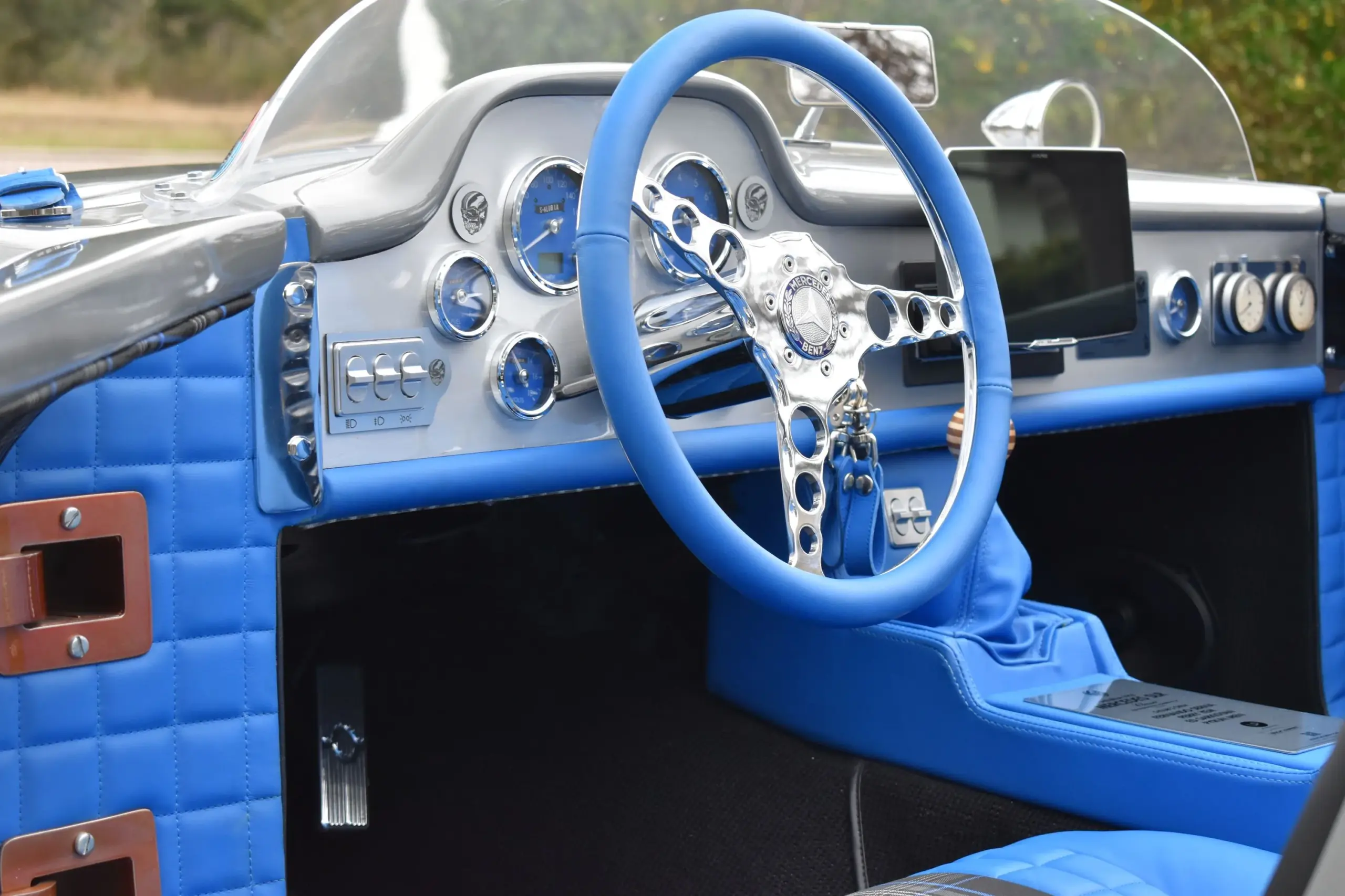 Nahaufnahme des Cockpits eines individuell gefertigten Roadsters mit blauem Leder, klassischen Rundinstrumenten und modernem Touchscreen.