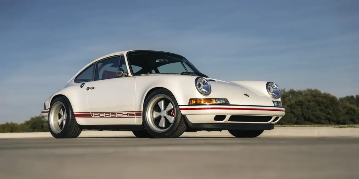 Weißer Porsche 911 Carrera Classic Study von Singer aus dem Jahr 1990 auf freier Fläche, Seitenansicht, dezente rote Akzente.