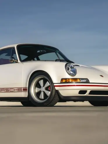 Weißer Porsche 911 Carrera Classic Study von Singer aus dem Jahr 1990 auf freier Fläche, Seitenansicht, dezente rote Akzente.