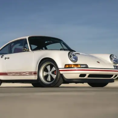 Weißer Porsche 911 Carrera Classic Study von Singer aus dem Jahr 1990 auf freier Fläche, Seitenansicht, dezente rote Akzente.