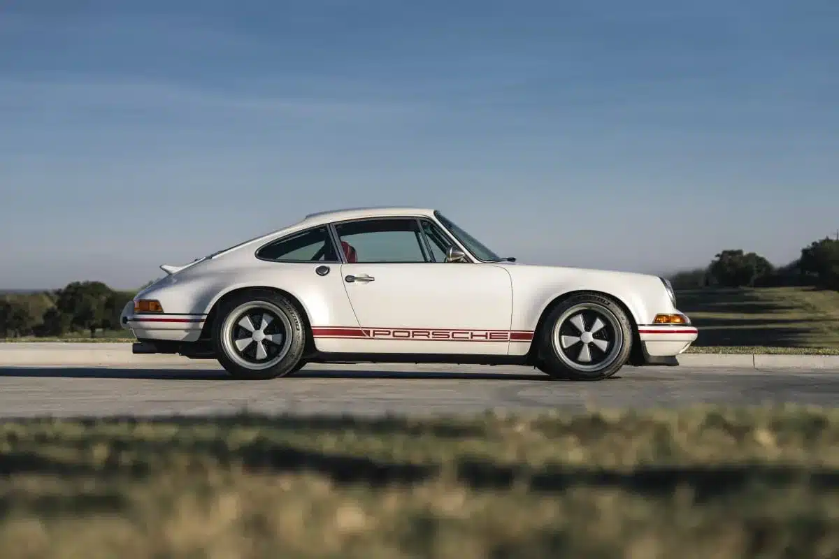 Seitenansicht eines silbernen Porsche 911 Carrera Classic Study von Singer mit rotem Porsche-Schriftzug auf einer Straße.