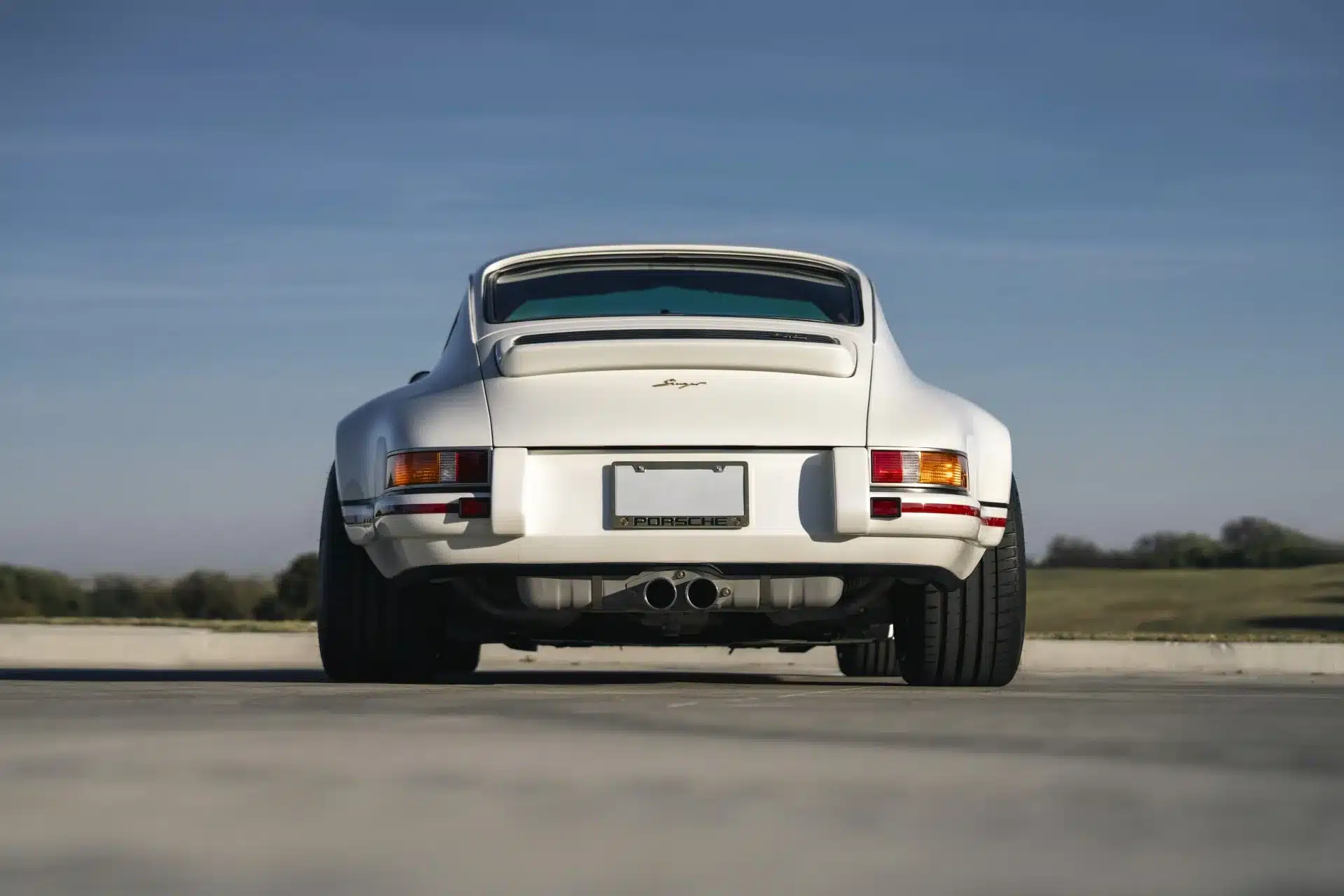 Heckansicht eines weißen Porsche 911 Carrera Classic Study by Singer aus den 1990er Jahren, aufgenommen auf einer Straße mit blauem Himmel