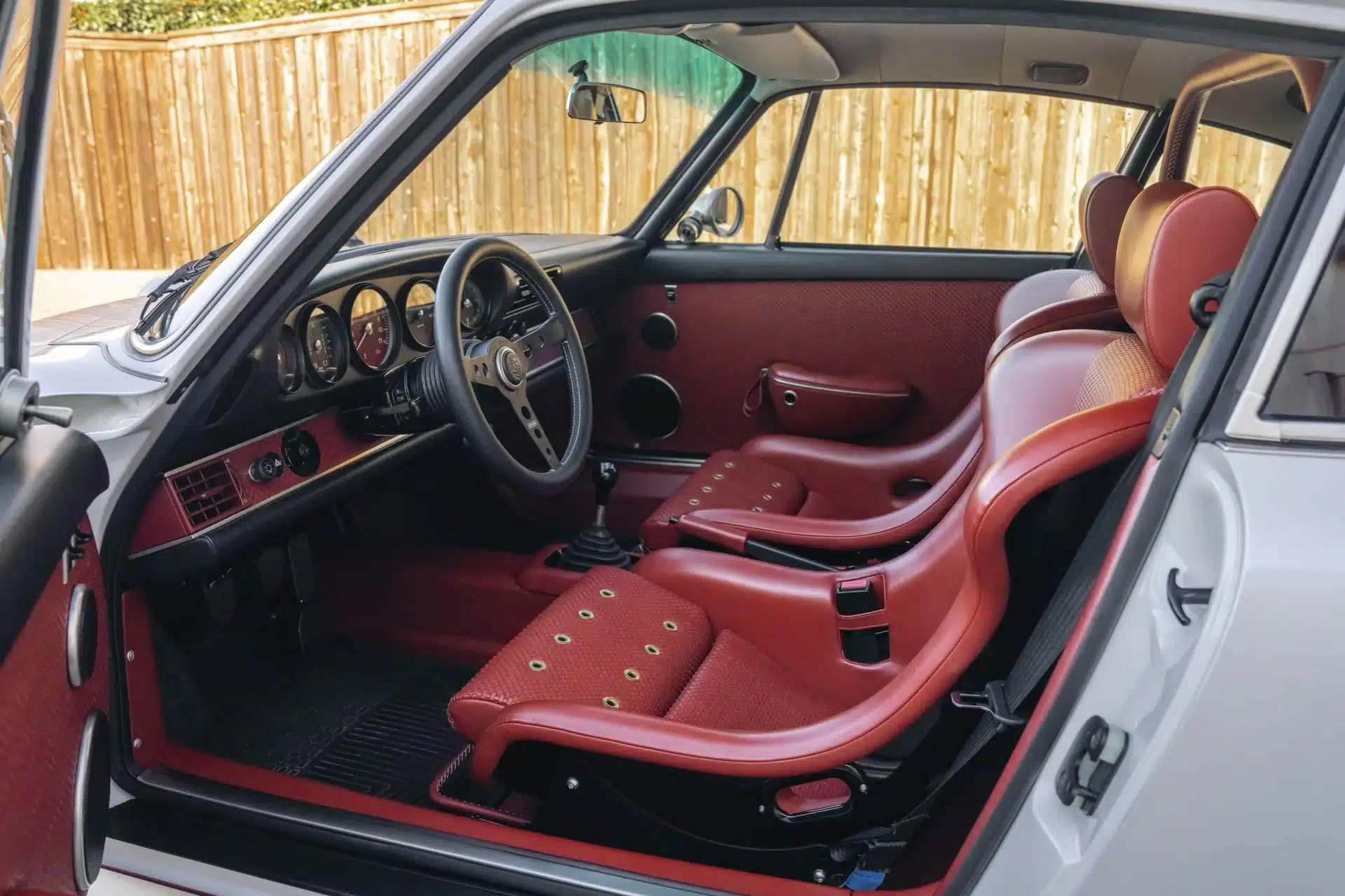 Innenraum eines 1990 Porsche 911 Carrera Classic Study by Singer, mit roten Sportsitzen und klassischen Rundinstrumenten.